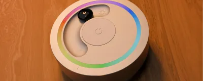 a light remote on a wooden table. The remote has a rainbow colored light ring, a marble in a slider and an on/off button.