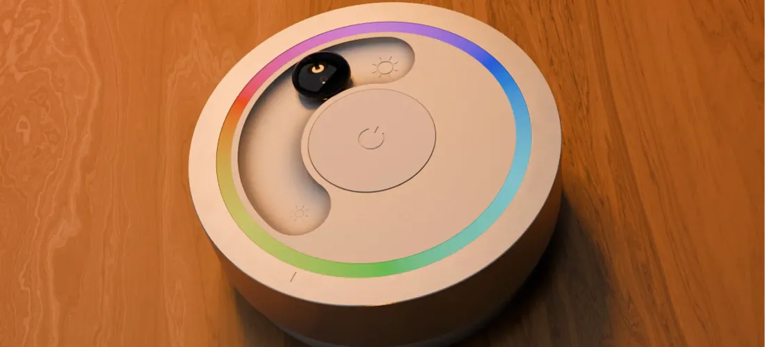 a light remote on a wooden table. The remote has a rainbow colored light ring, a marble in a slider and an on/off button.